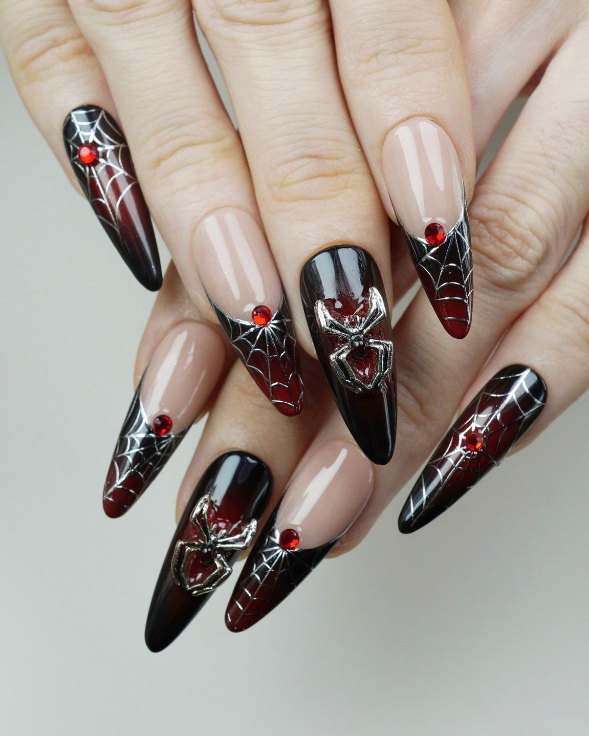 Long sheer nude stiletto nails feature black and red graphic motifs with small metallic-looking accents.