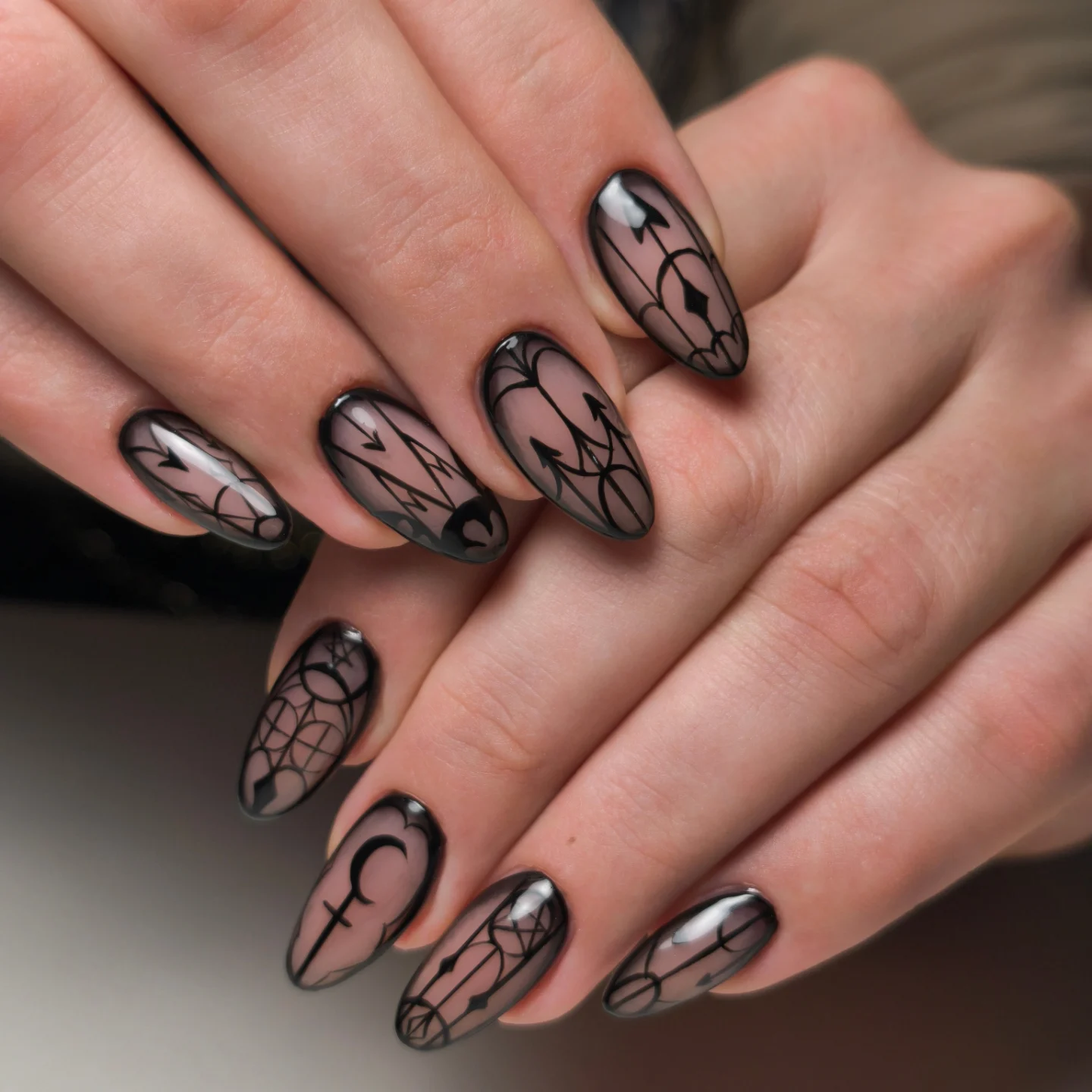 Almond-shaped nude nails are outlined with delicate black spiderweb and gothic line designs.