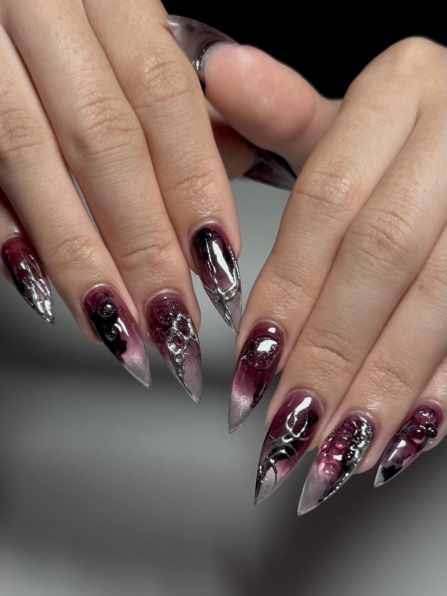 Pointed sheer nude nails are accented with deep red and black decorative sections for a dark finish.
