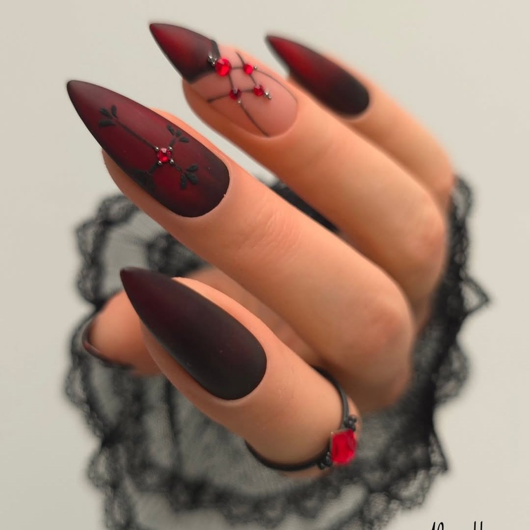 Pointed nails combine deep red and black sections in a sleek, moody Halloween palette.