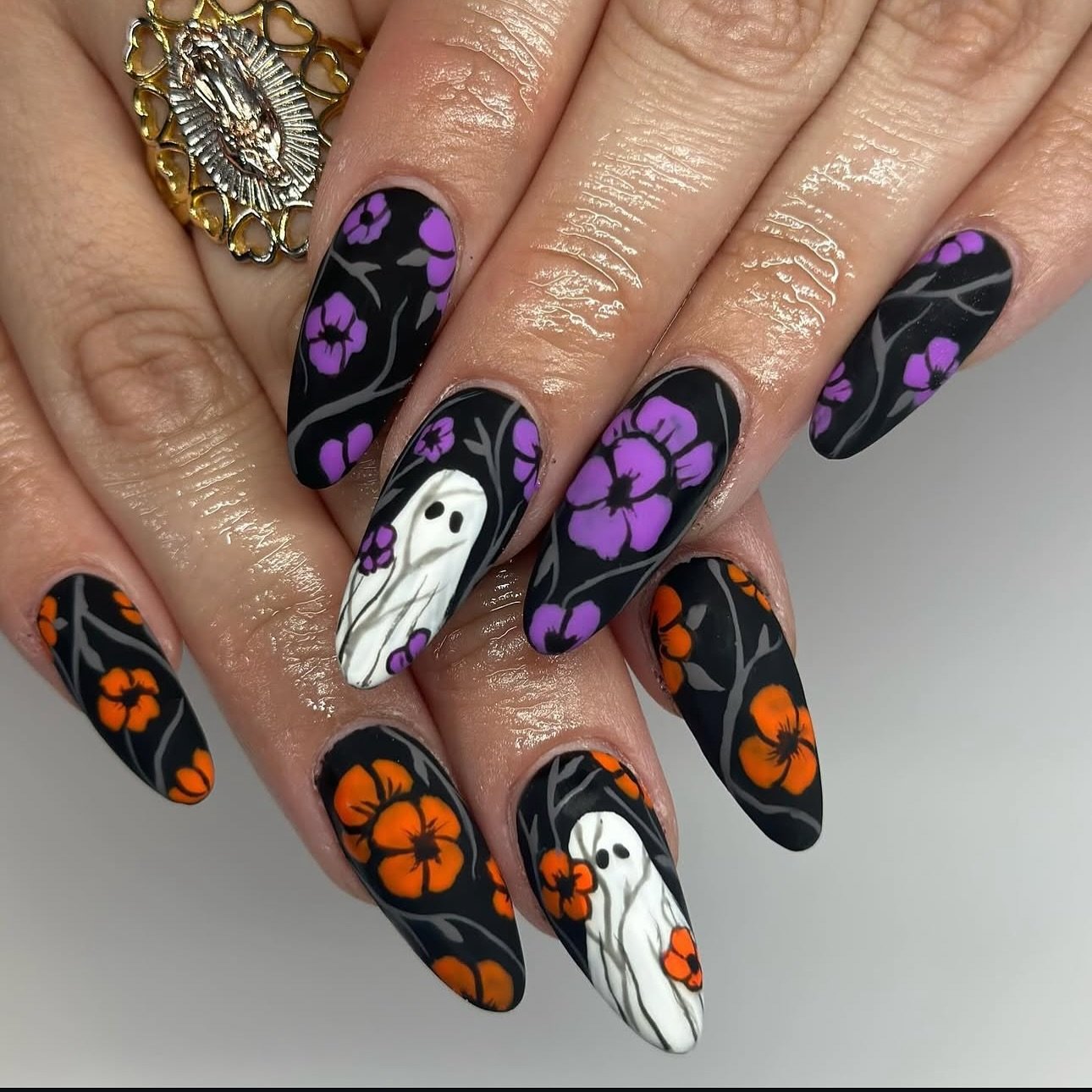 Long black almond Halloween nails with purple flowers, orange pumpkins, and white ghosts.