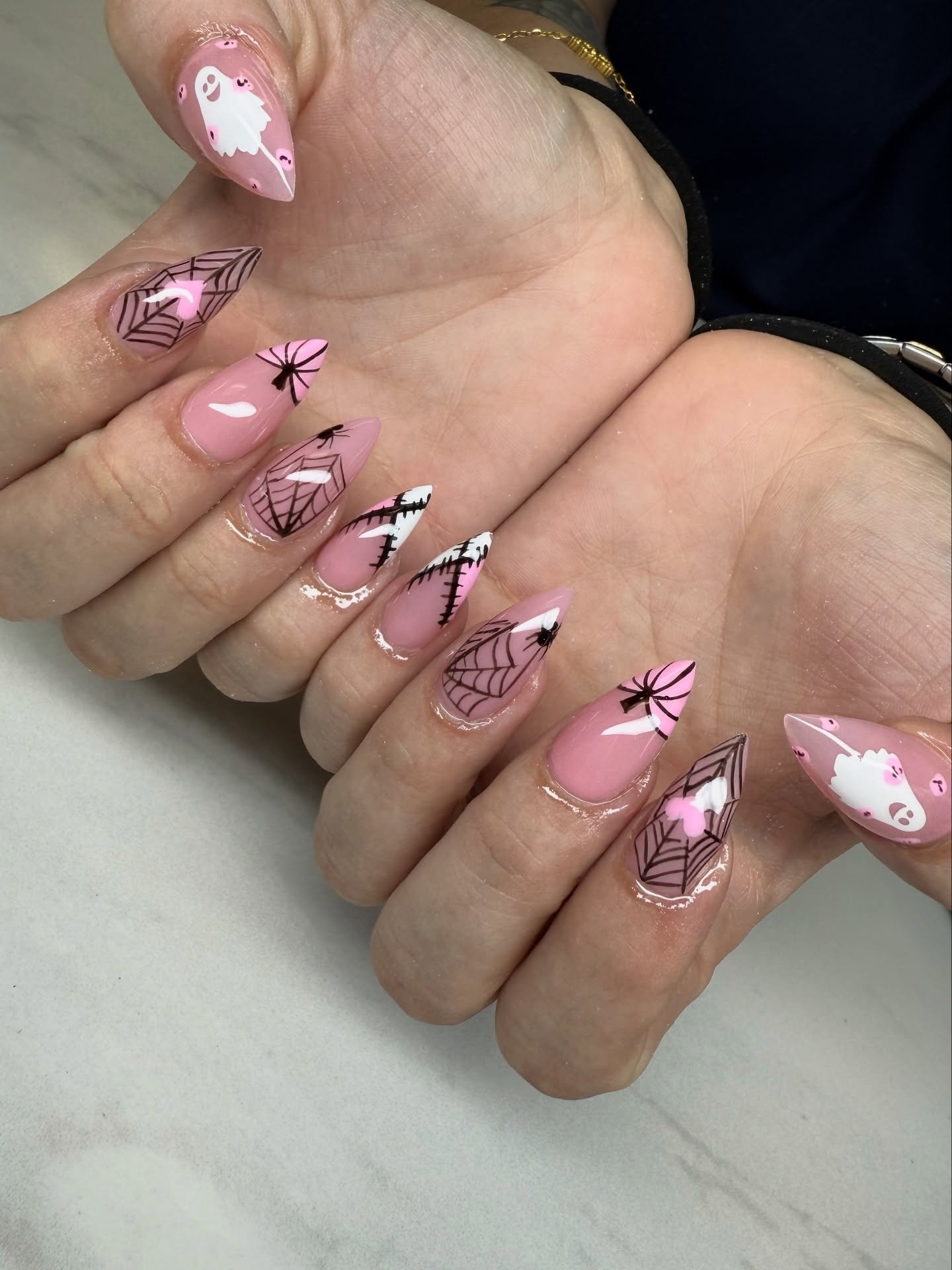 Pink almond Halloween nails with spiderwebs, bats, and ghosts.