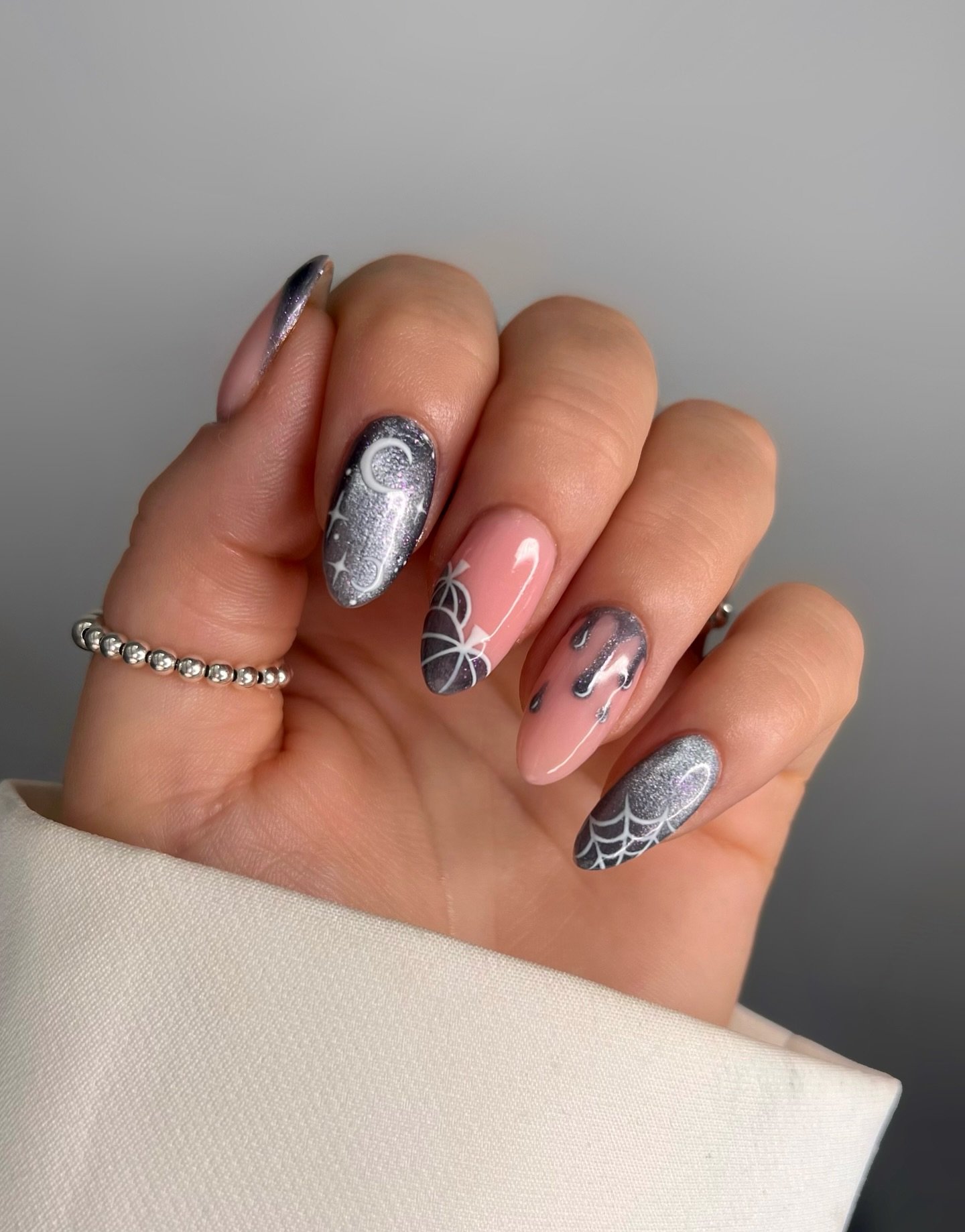 Pink and silver almond Halloween nails with black spiderweb details.