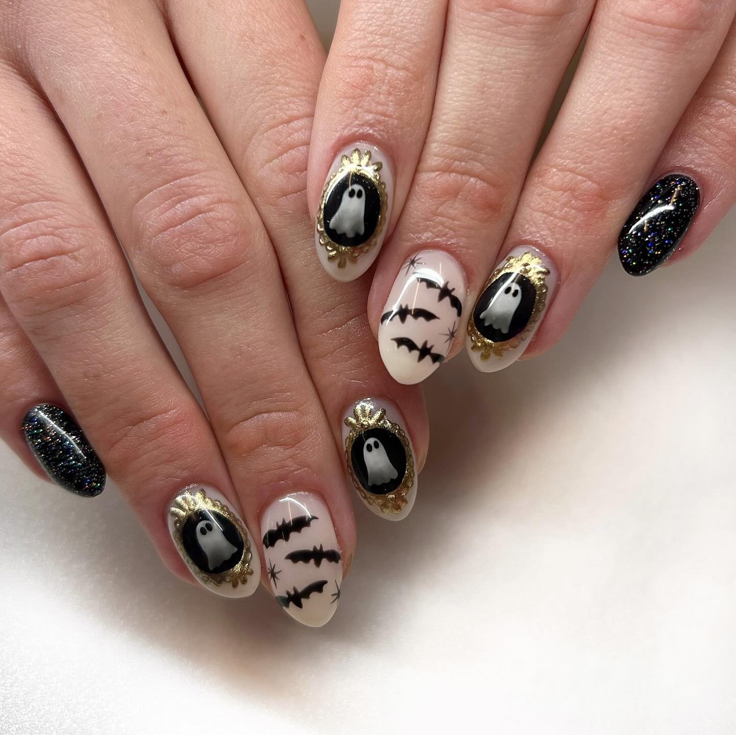 Pink almond Halloween nails with gold-framed ghosts, bats, and black glitter.