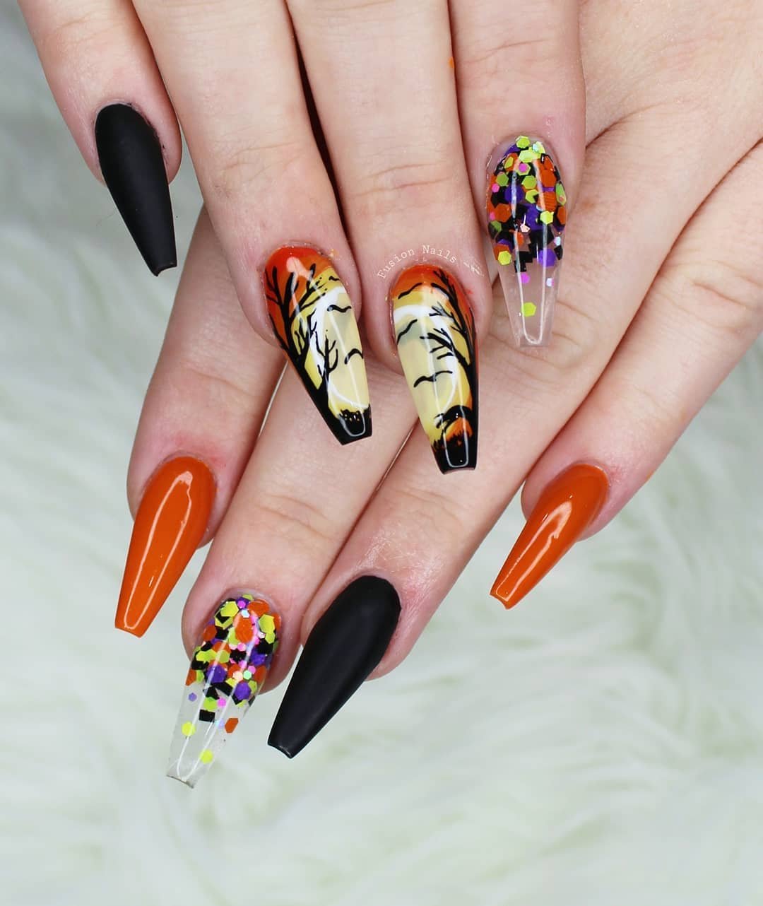 Orange and black coffin Halloween nails with confetti and tiger-stripe accents.