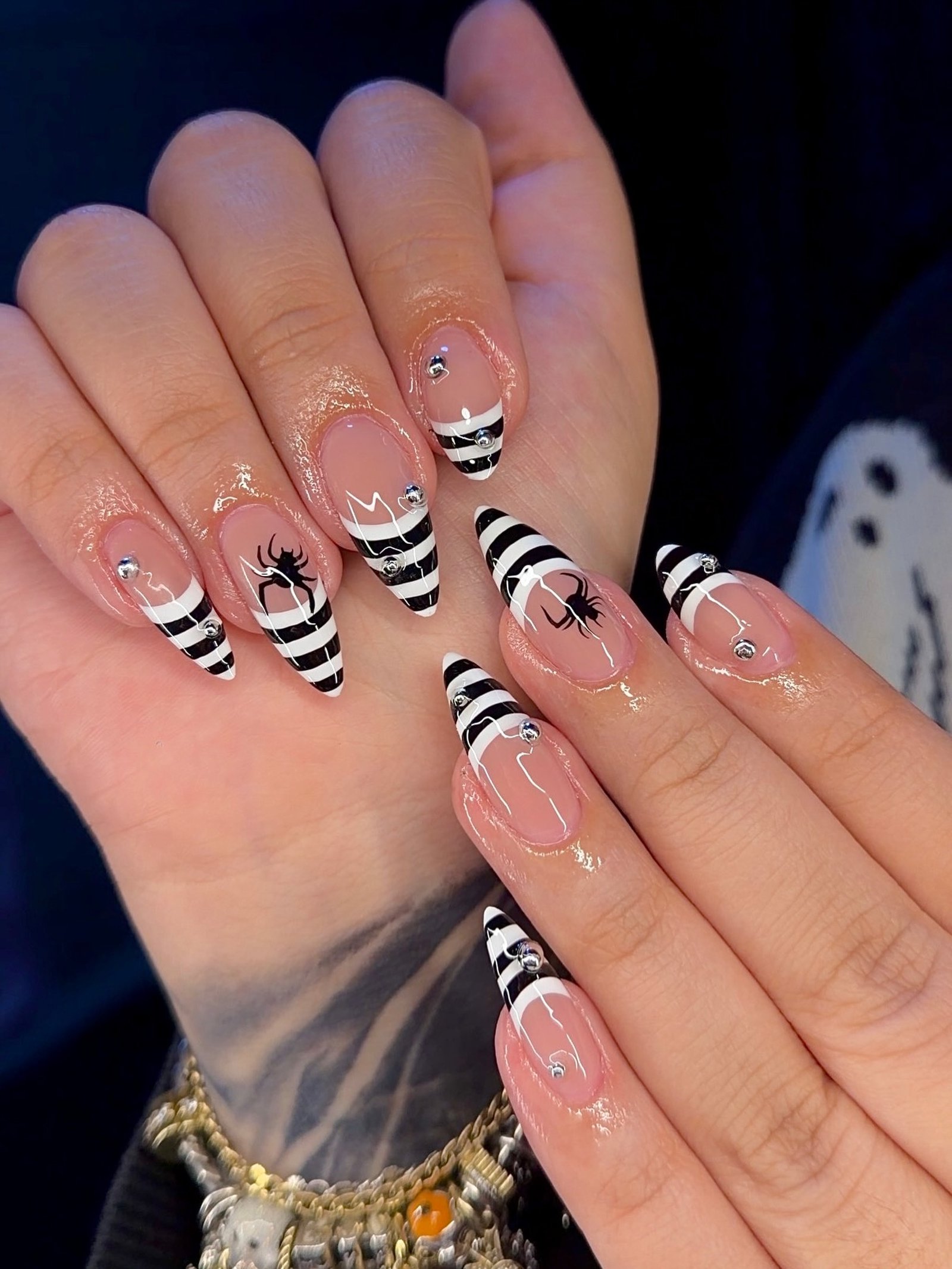 Nude almond Halloween nails with black-and-white striped tips and spiders.