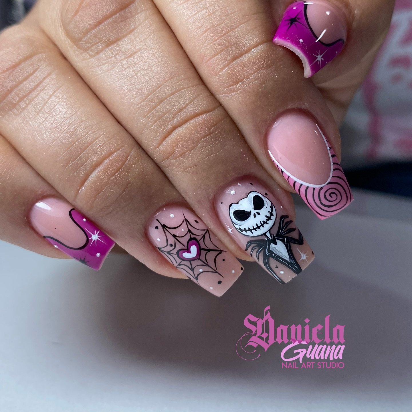 Pink and black square Halloween nails with spiderwebs and a Jack Skellington-style character.