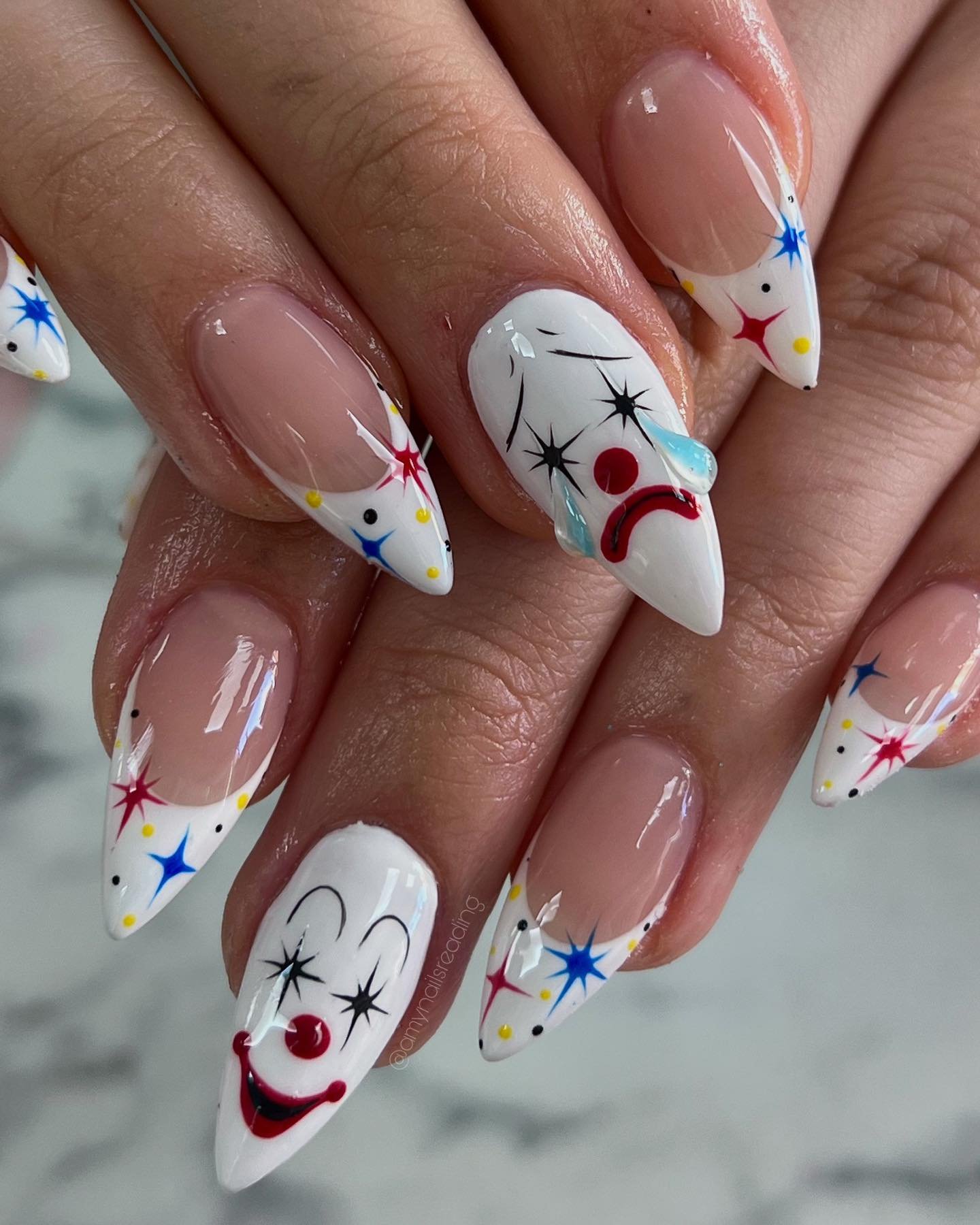 Almond Halloween nails with colorful starbursts and a red-and-white clown face.