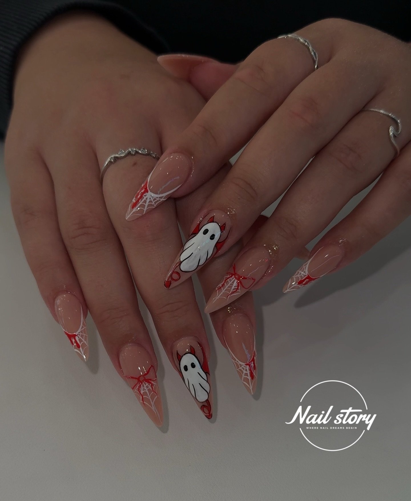 Sheer pink stiletto Halloween nails with ghosts and red spiderweb tips.