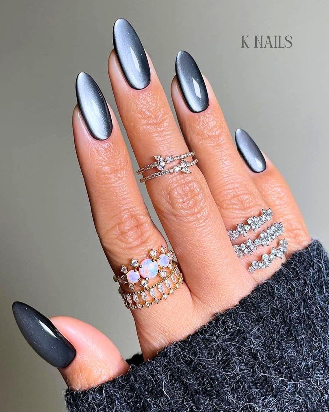 Long stiletto nails feature a reflective silver-blue cat-eye effect across a smooth, dark metallic base.