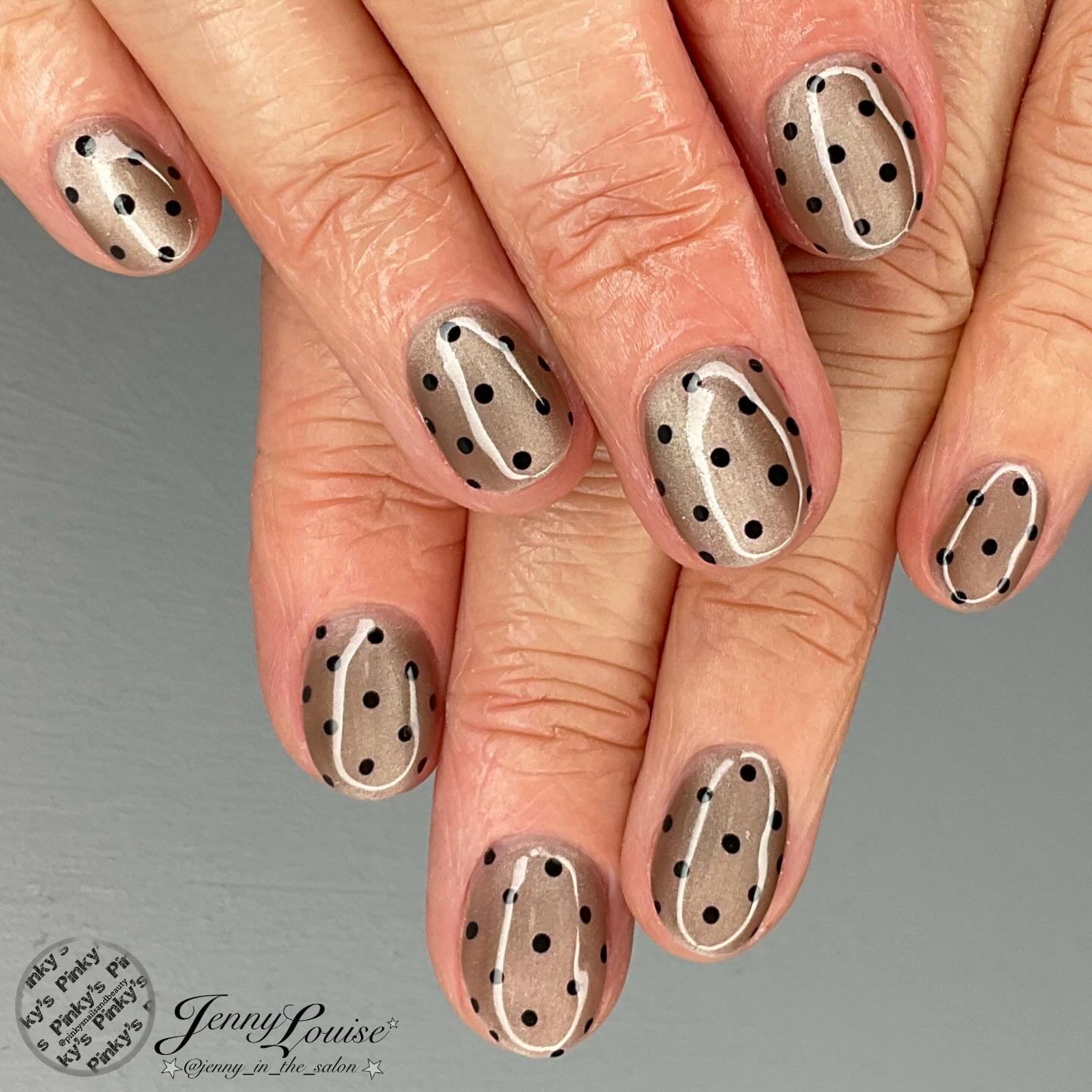 Short oval taupe-beige nails are finished with evenly spaced black dots and thin black outlining details.