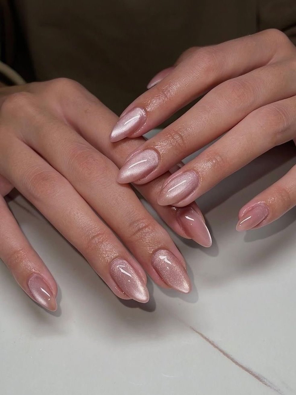 Long almond nails use a sheer pink base with a clean glossy finish and subtle natural-looking variation.