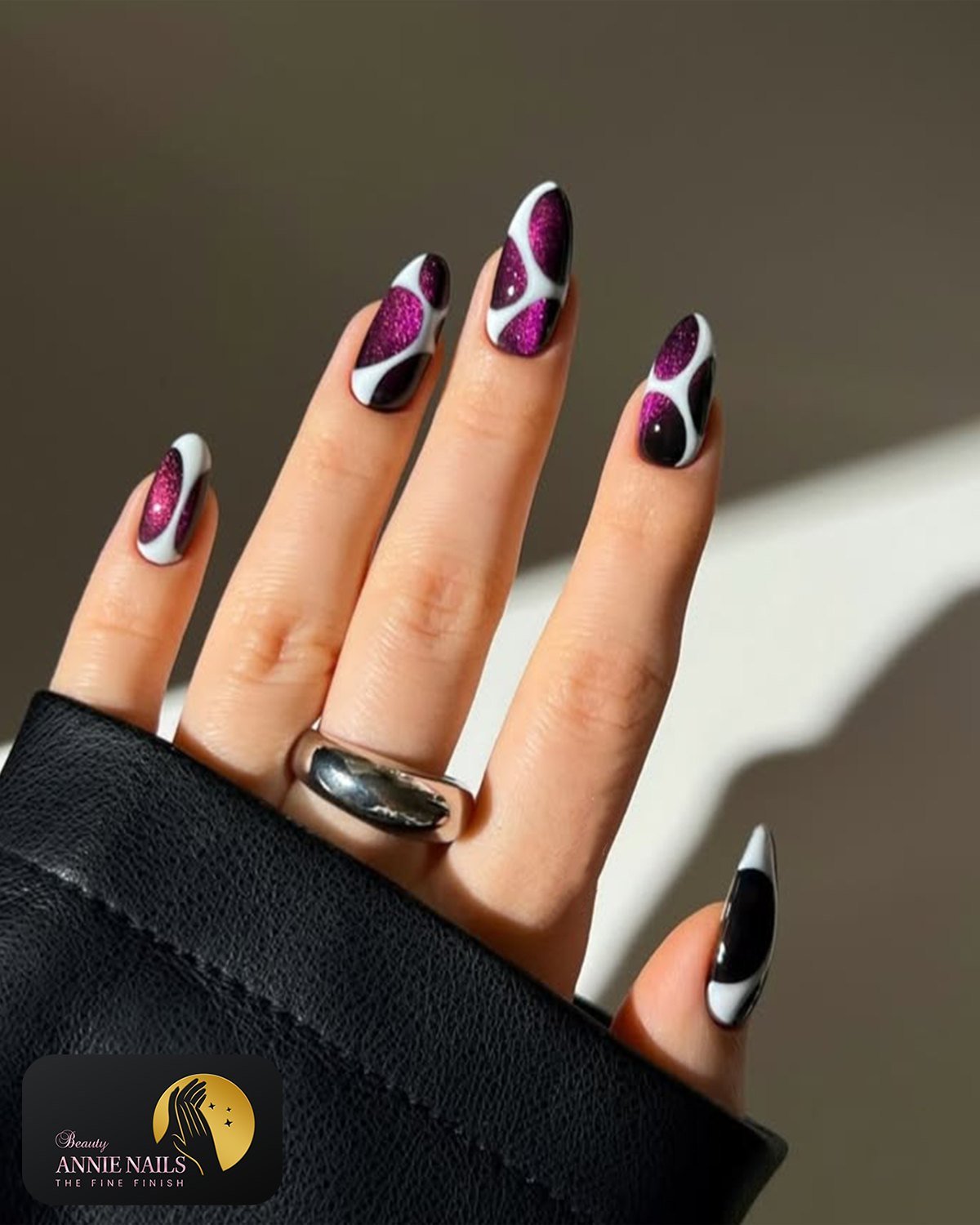 Long almond nails have a black base decorated with vivid pink and purple curved accents near the tips and sides.