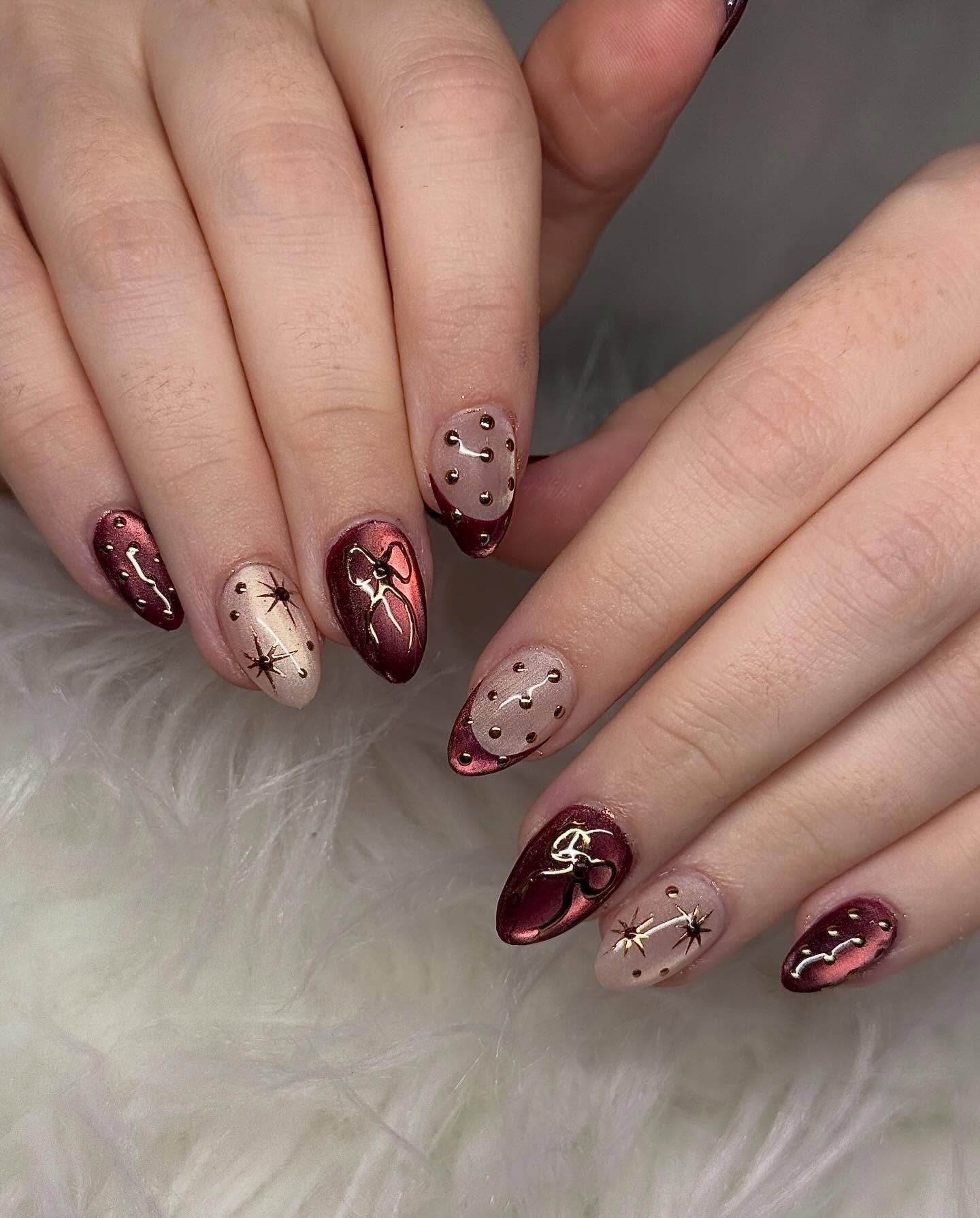Medium almond nails mix glossy burgundy with nude-toned nails decorated by small dark accent details.