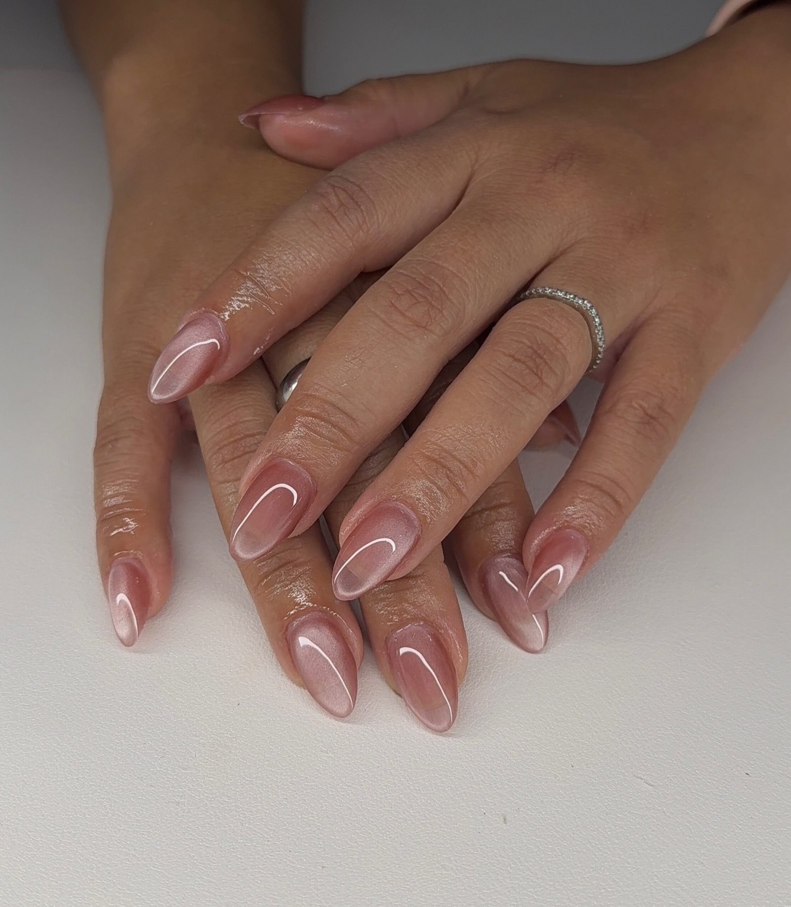 Medium-to-long almond nails use a sheer pink base with delicate white curved lines and a glossy finish.