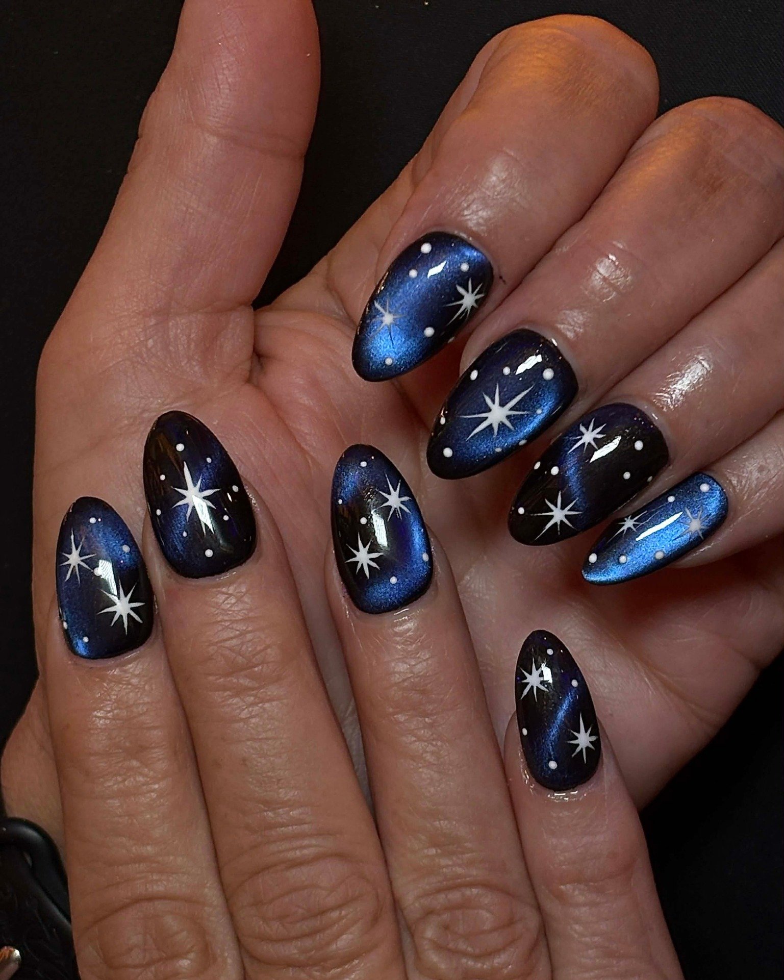 Medium oval nails are glossy navy blue, with several nails accented by crisp white starburst designs.