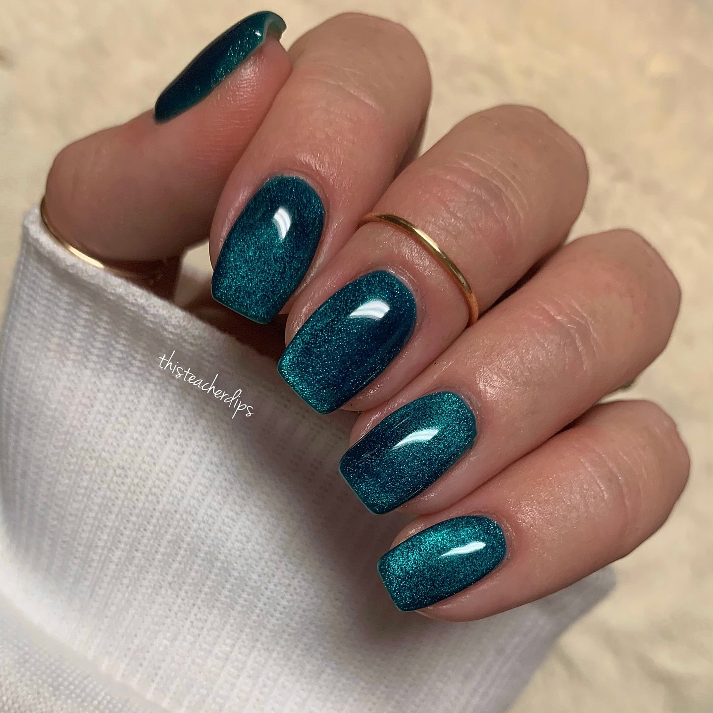 Short square nails are coated in a deep teal shade with a strong luminous velvet-like shimmer.