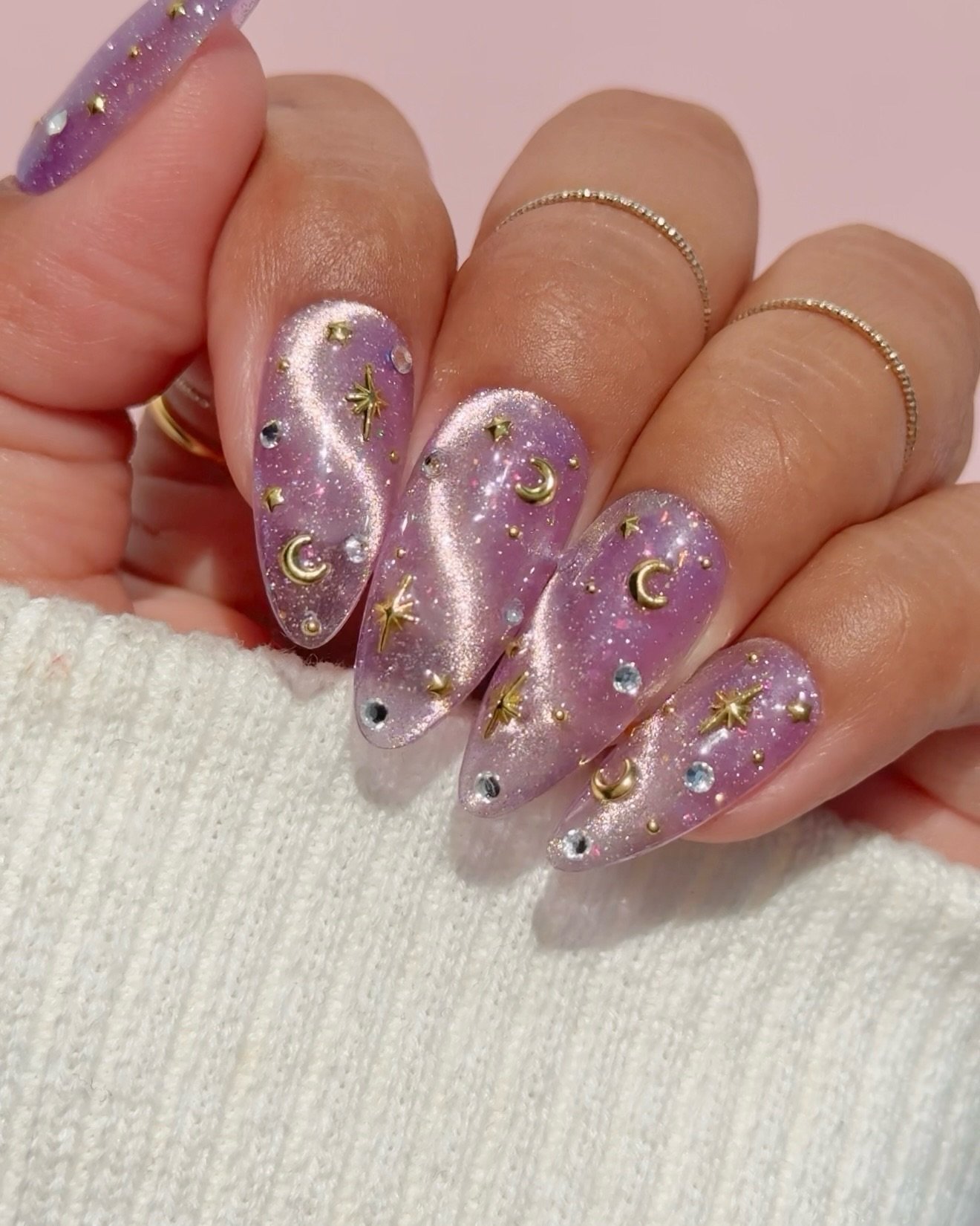 Long almond nails combine pink and cream tones with ornate gold embellishments and textured decorative accents.