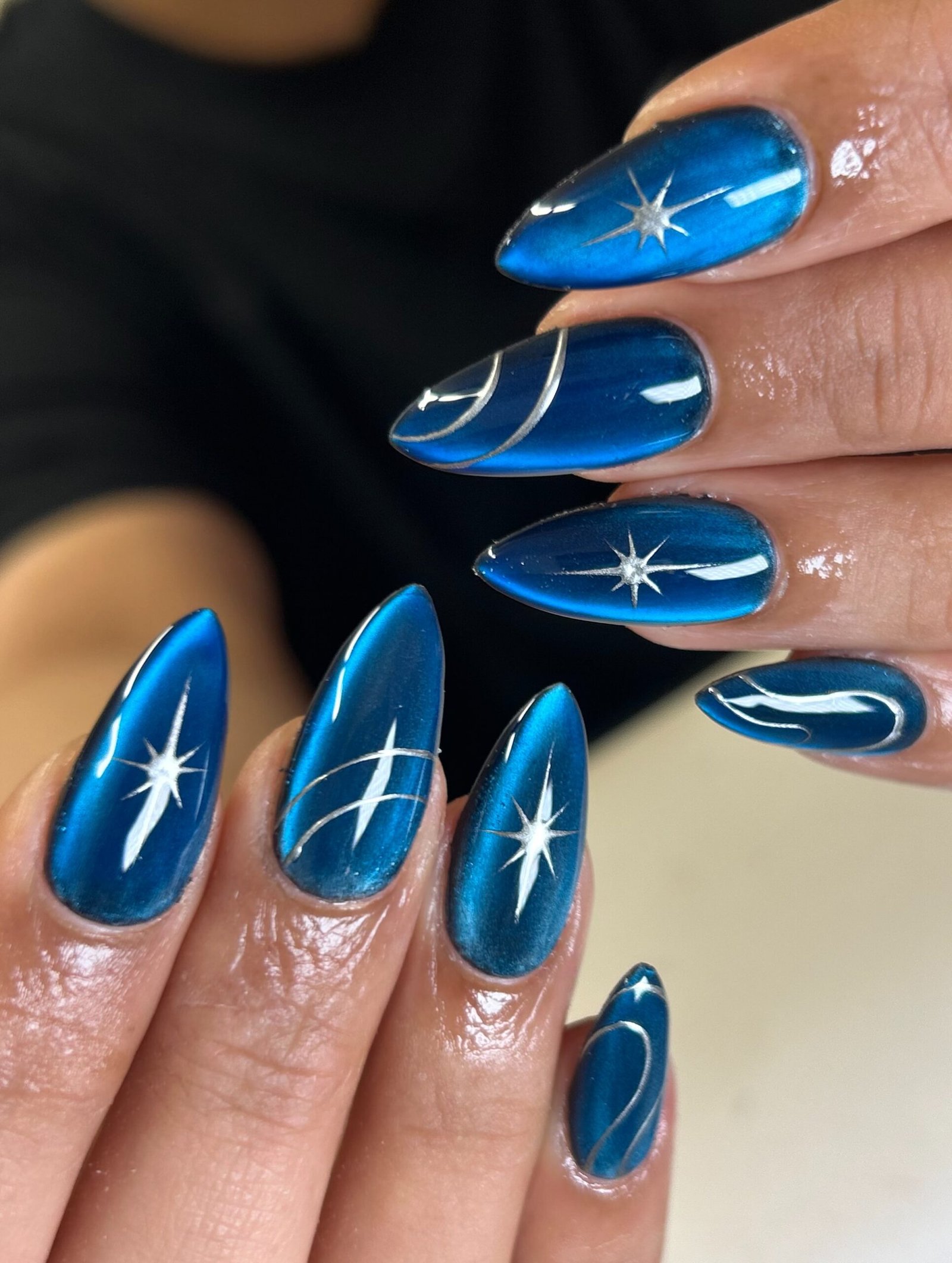 Short-to-medium oval nails use a brown-taupe base with pale reflective linework creating a luminous patterned effect.