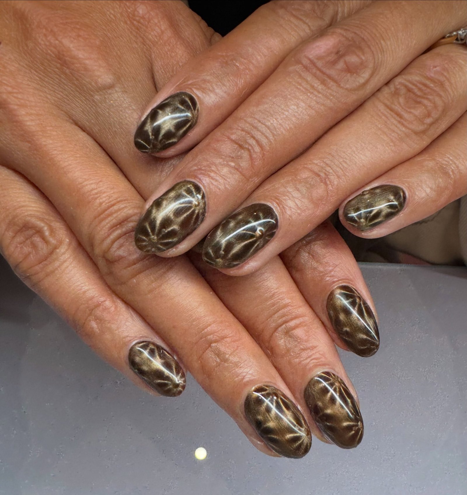 Short rounded nails have a sheer nude base with dark green French tips, thin gold accents, and black-and-white linework.