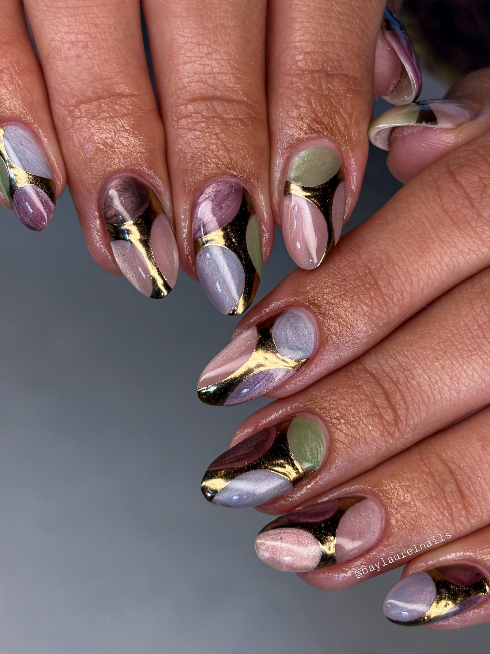 Long almond nails combine lavender, taupe, soft pink, and pale green sections separated by bold reflective gold bands.